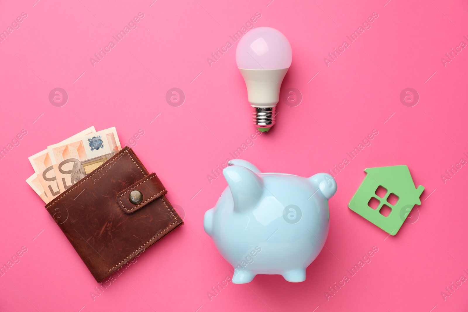 Photo of Piggy bank, light bulb, house model and purse with euro banknotes on pink background, flat lay. Energy saving concept