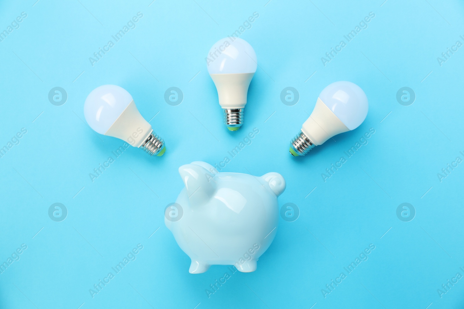 Photo of Piggy bank and lightbulbs on light blue background, flat lay. Energy saving concept