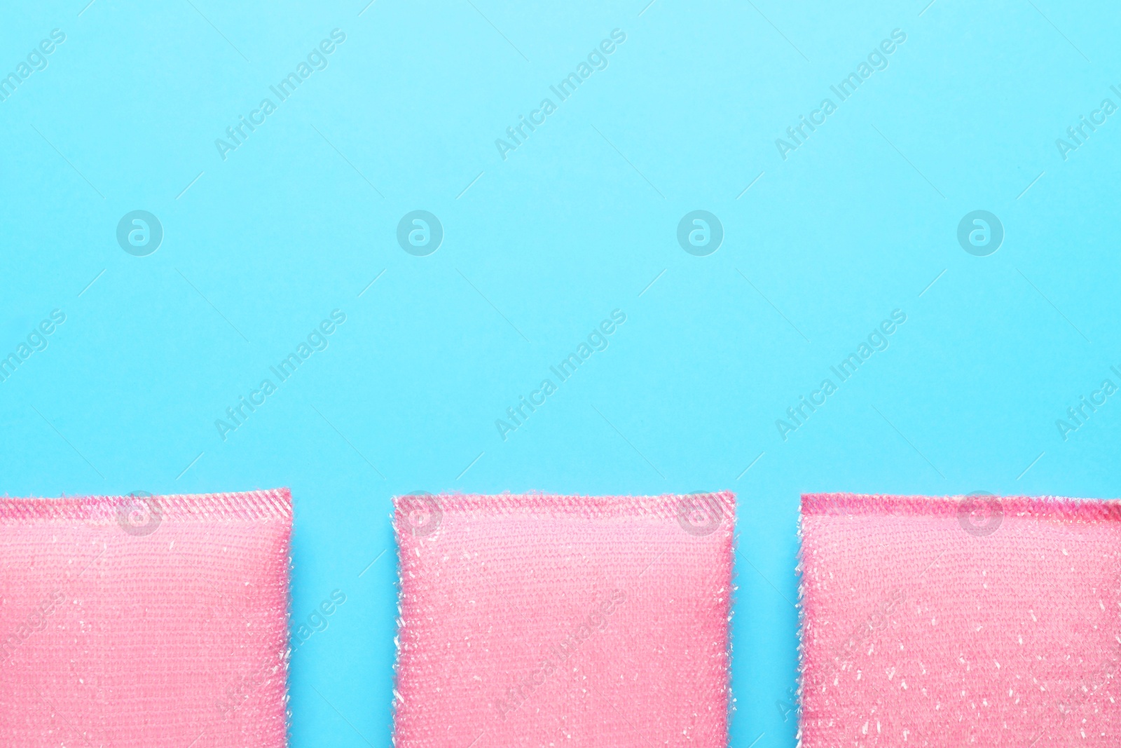 Photo of Pink sponges on light blue background, flat lay. Space for text