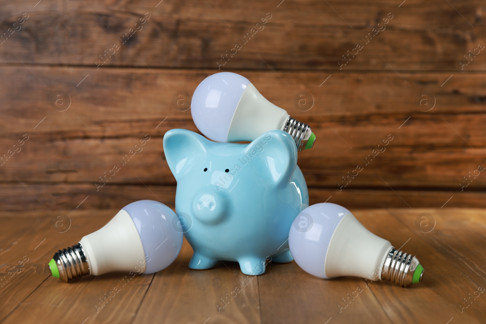 Photo of Piggy bank and light bulbs on wooden table. Energy saving concept