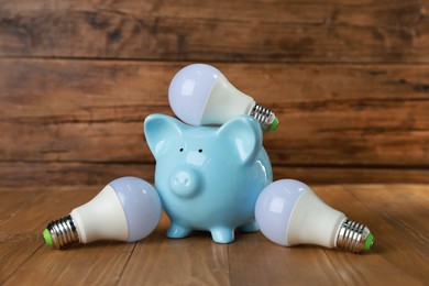 Photo of Piggy bank and light bulbs on wooden table. Energy saving concept