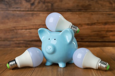 Photo of Piggy bank and light bulbs on wooden table. Energy saving concept