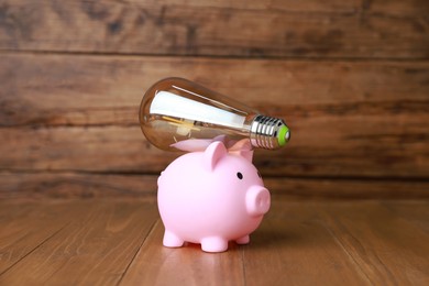 Photo of Piggy bank and light bulb on wooden table. Energy saving concept