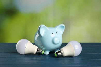 Photo of Piggy bank and light bulbs on blue wooden table outdoors. Energy saving concept