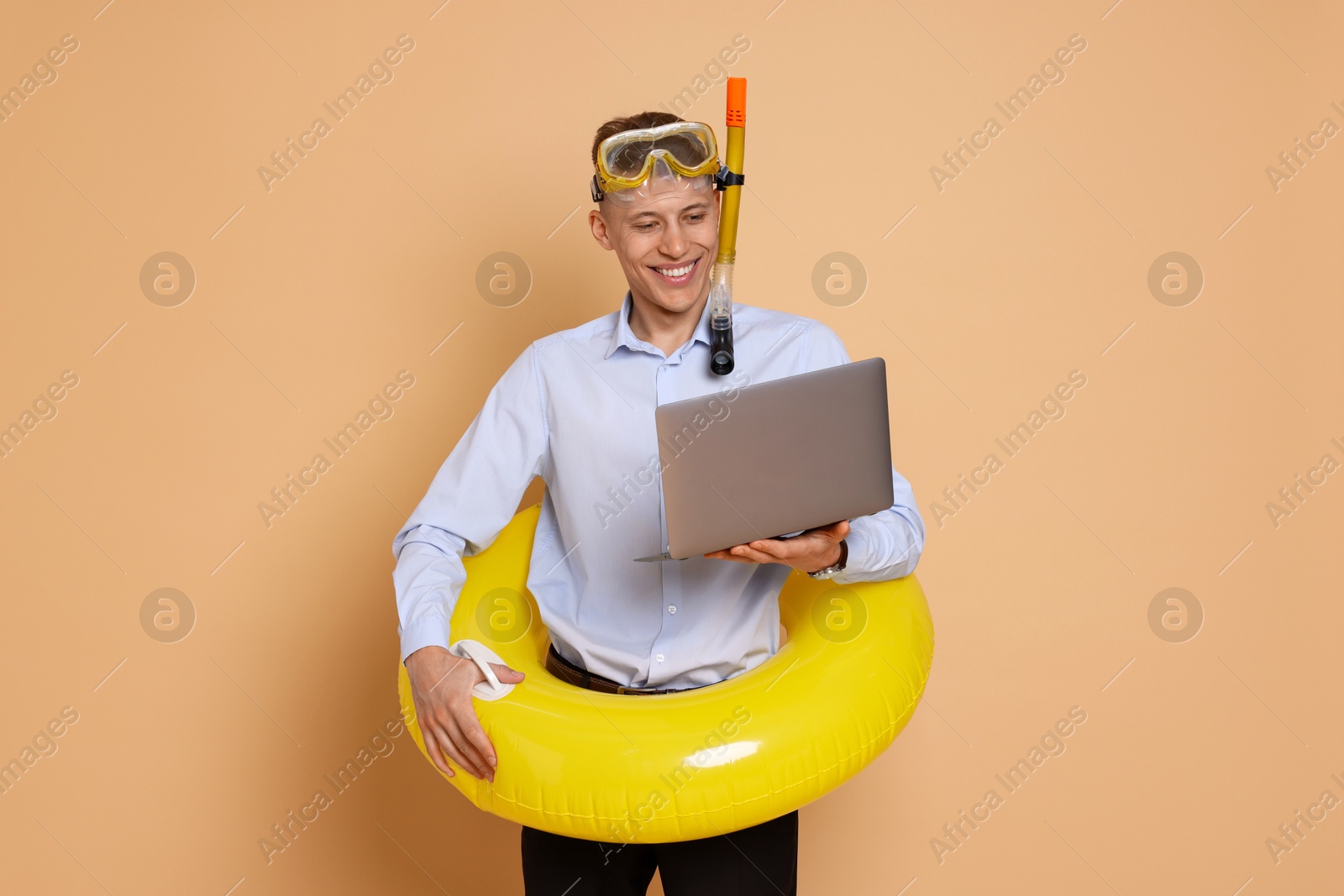 Photo of Businessman with inflatable ring, laptop and snorkeling equipment on beige background