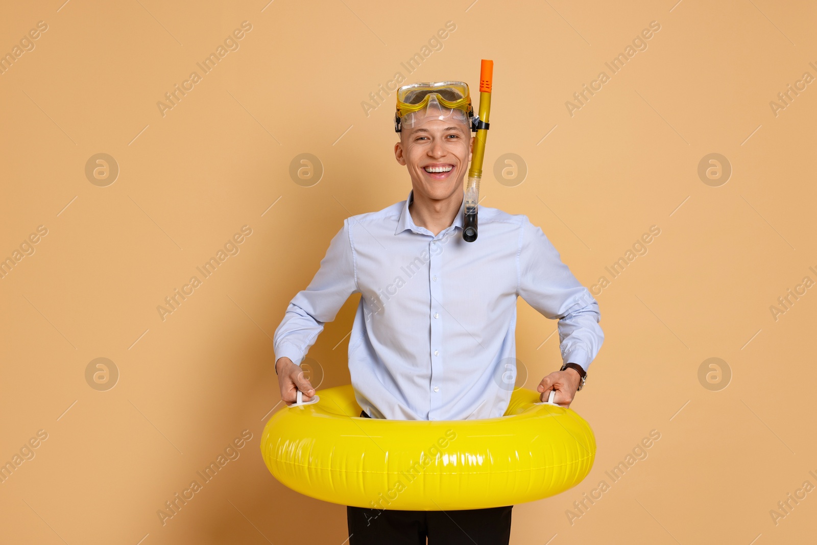 Photo of Businessman with inflatable ring and snorkeling equipment on beige background