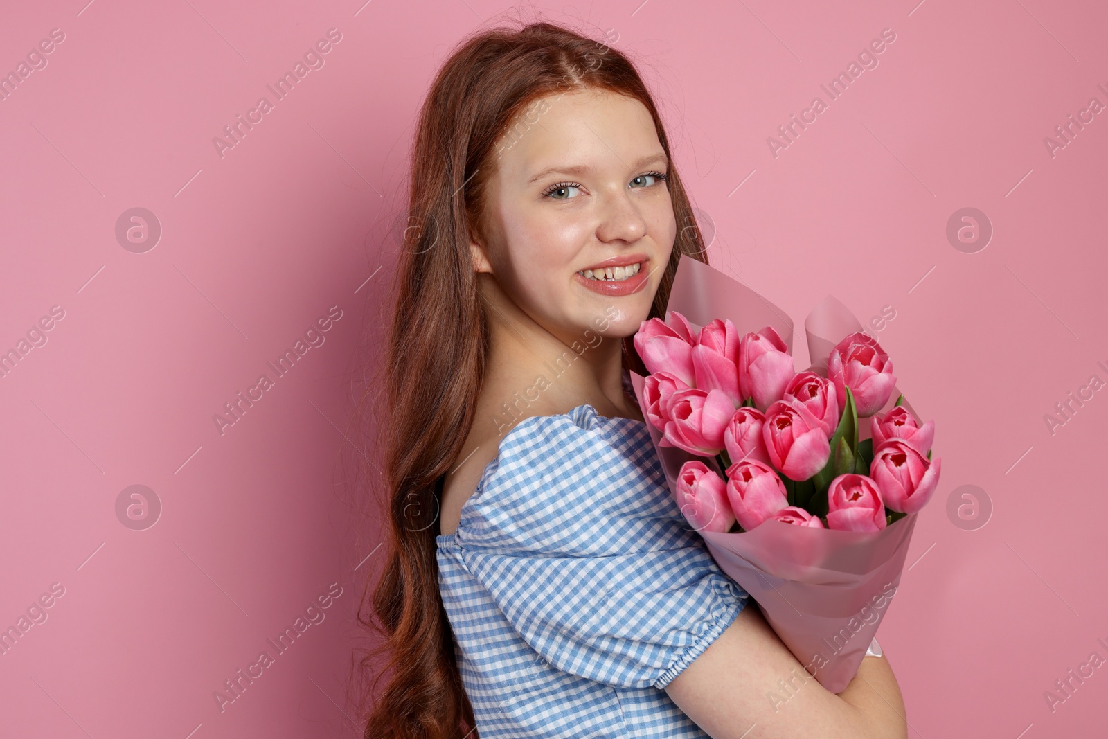 Photo of Beautiful teenage girl with bouquet of tulips on pink background