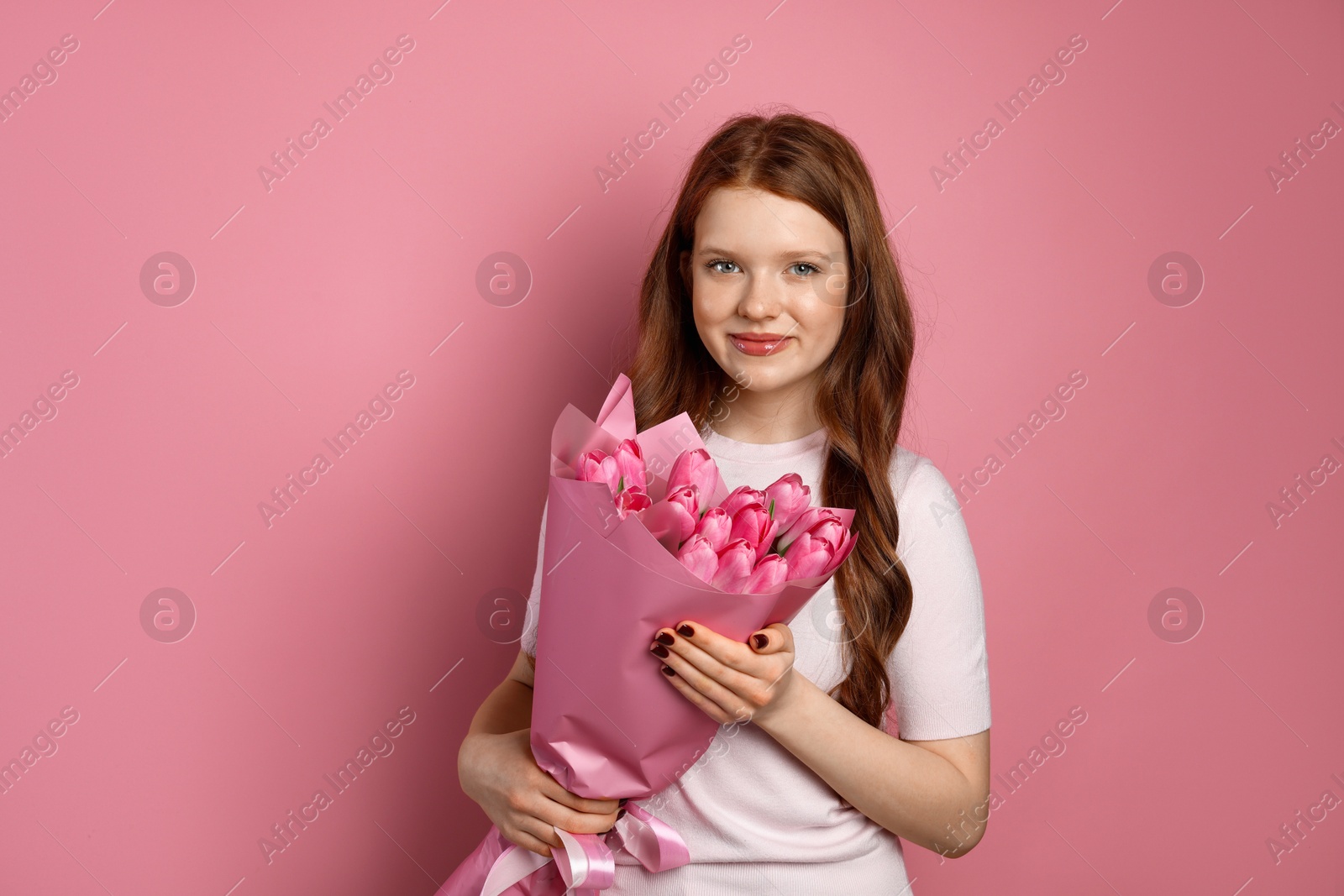 Photo of Beautiful teenage girl with bouquet of tulips on pink background