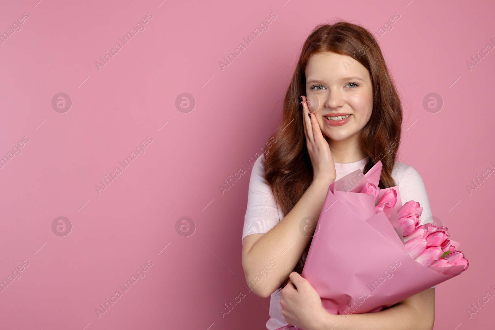 Photo of Beautiful teenage girl with bouquet of tulips on pink background, space for text