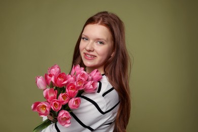 Photo of Beautiful teenage girl with bouquet of tulips on olive background