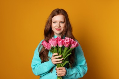 Photo of Beautiful teenage girl with bouquet of tulips on orange background