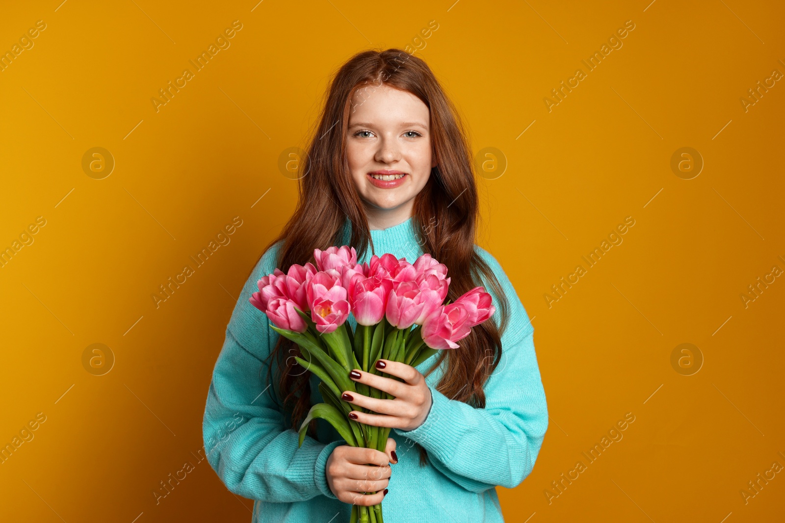 Photo of Beautiful teenage girl with bouquet of tulips on orange background