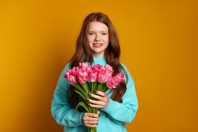 Photo of Beautiful teenage girl with bouquet of tulips on orange background