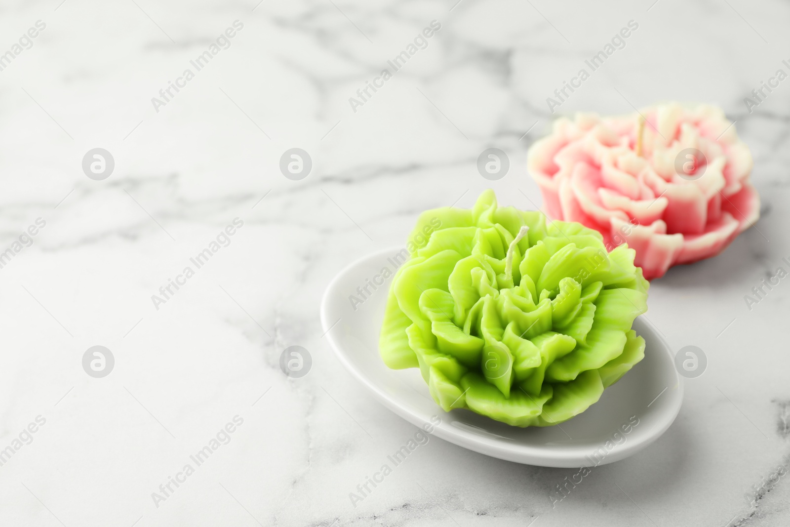 Photo of Beautiful flower shaped candles on white marble background, closeup. Space for text