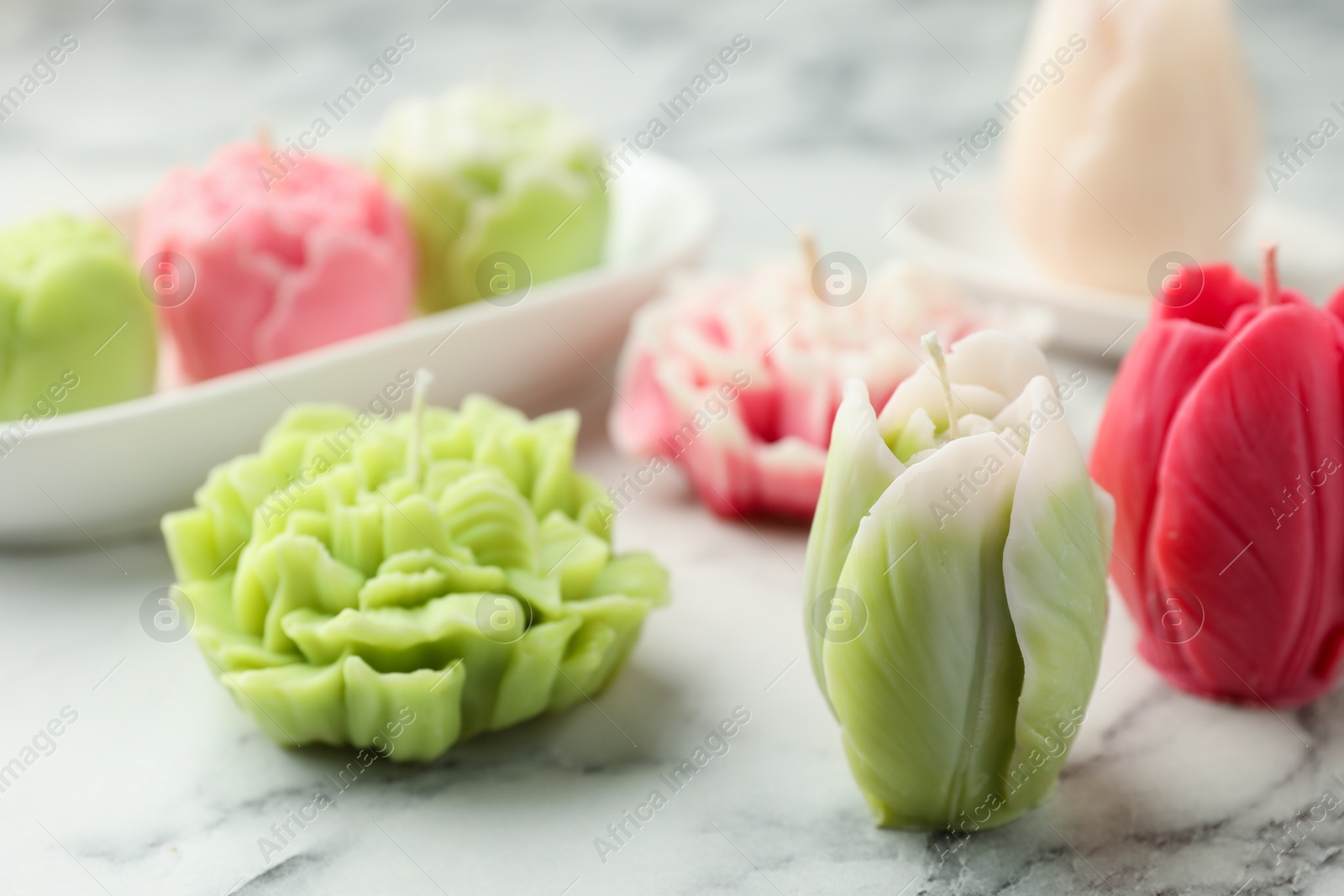 Photo of Beautiful flower shaped candles on white marble background, closeup