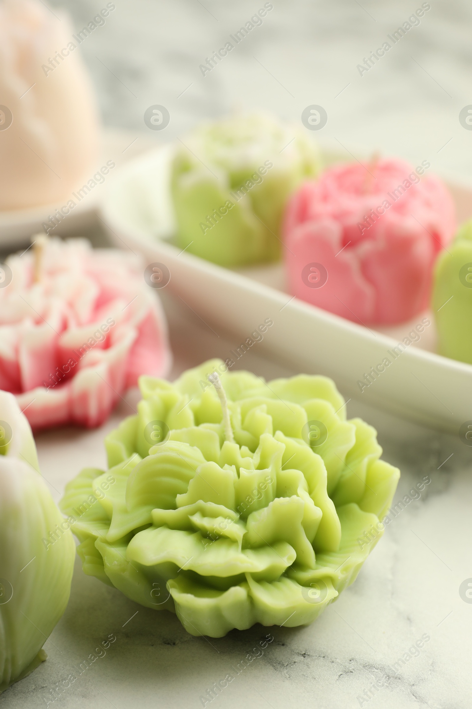 Photo of Beautiful flower shaped candles on white marble background, closeup