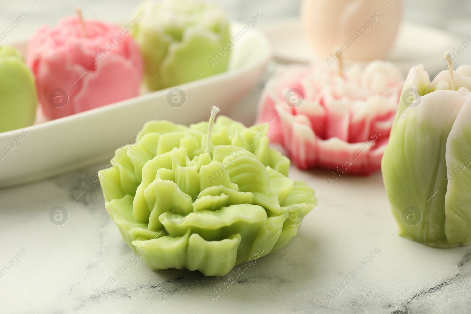 Photo of Beautiful flower shaped candles on white marble background, closeup