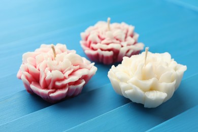 Photo of Beautiful flower shaped candles on blue wooden background, closeup