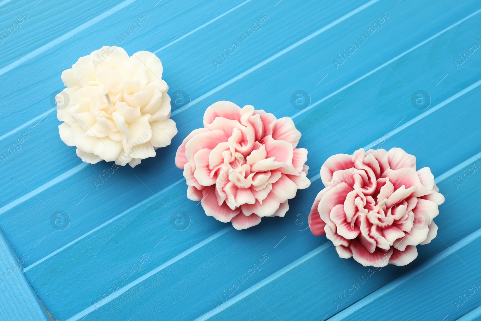 Photo of Beautiful flower shaped candles on blue wooden background, flat lay