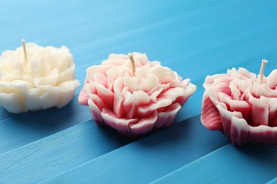 Photo of Beautiful flower shaped candles on blue wooden background, closeup