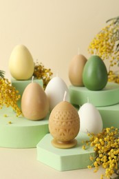 Photo of Beautiful egg shaped candles and mimosa flowers on beige background. Easter decor