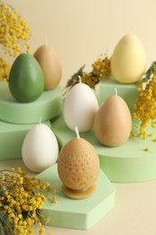 Photo of Beautiful egg shaped candles and mimosa flowers on beige background. Easter decor