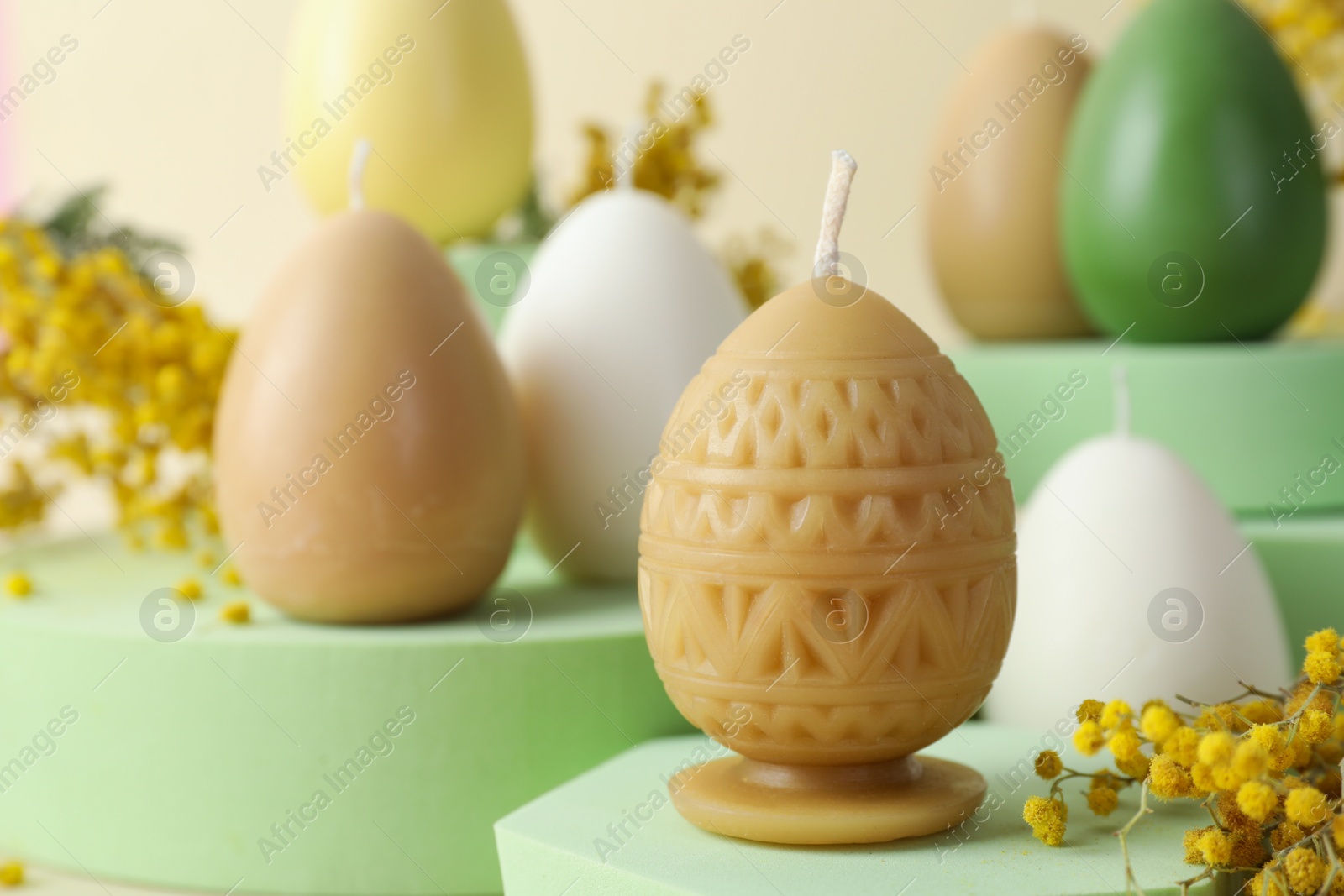 Photo of Beautiful egg shaped candles and mimosa flowers on beige background, closeup. Easter decor