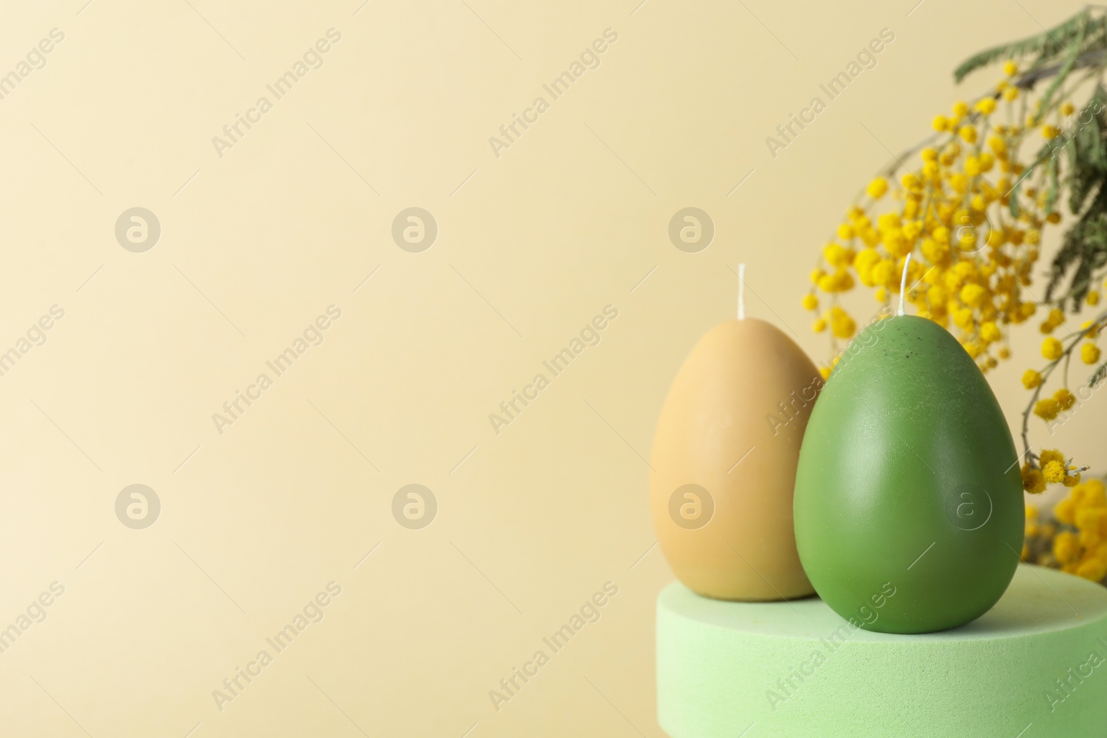 Photo of Beautiful egg shaped candles and mimosa flowers on beige background, closeup with space for text. Easter decor