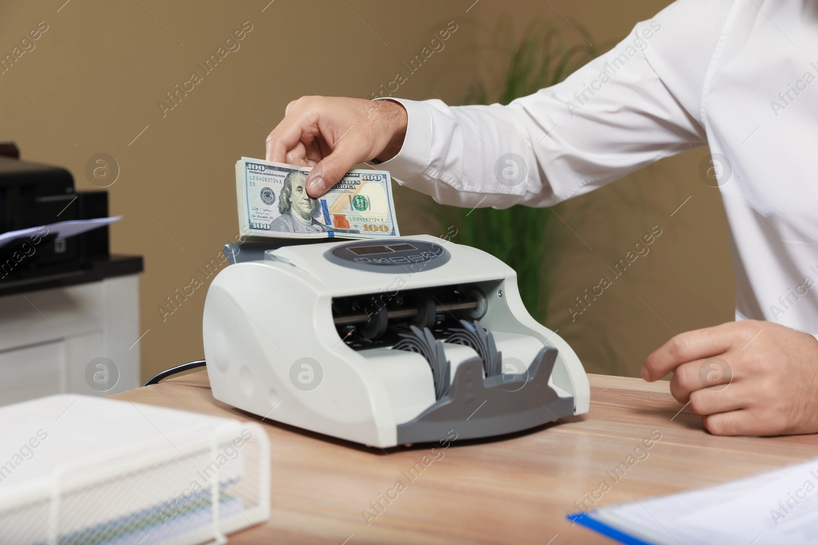 Photo of Man putting money into banknote counter at wooden table indoors, closeup