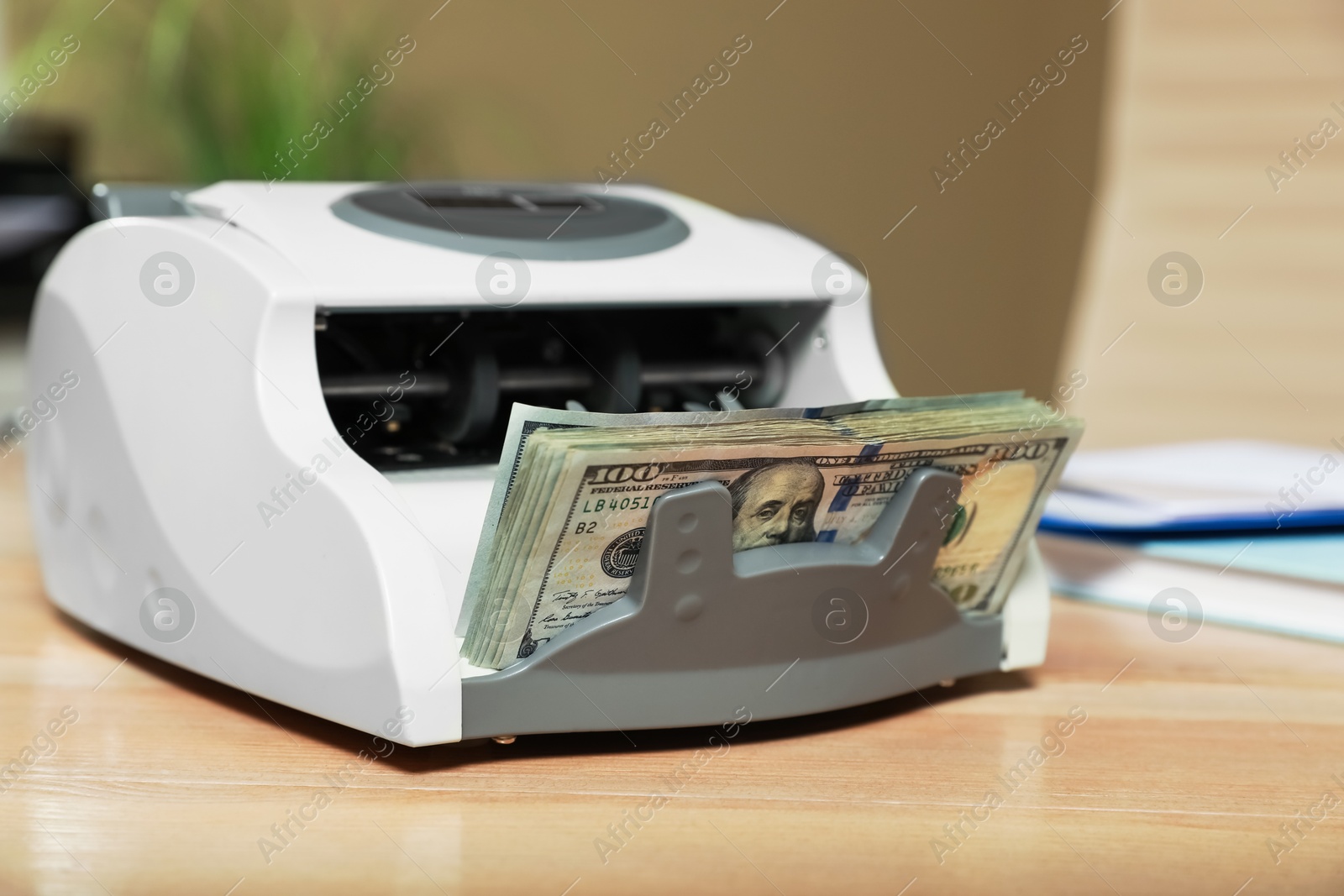 Photo of Modern banknote counter with money on wooden table indoors, closeup