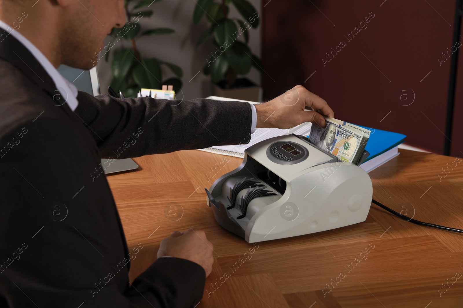 Photo of Man putting money into banknote counter at wooden table indoors, closeup