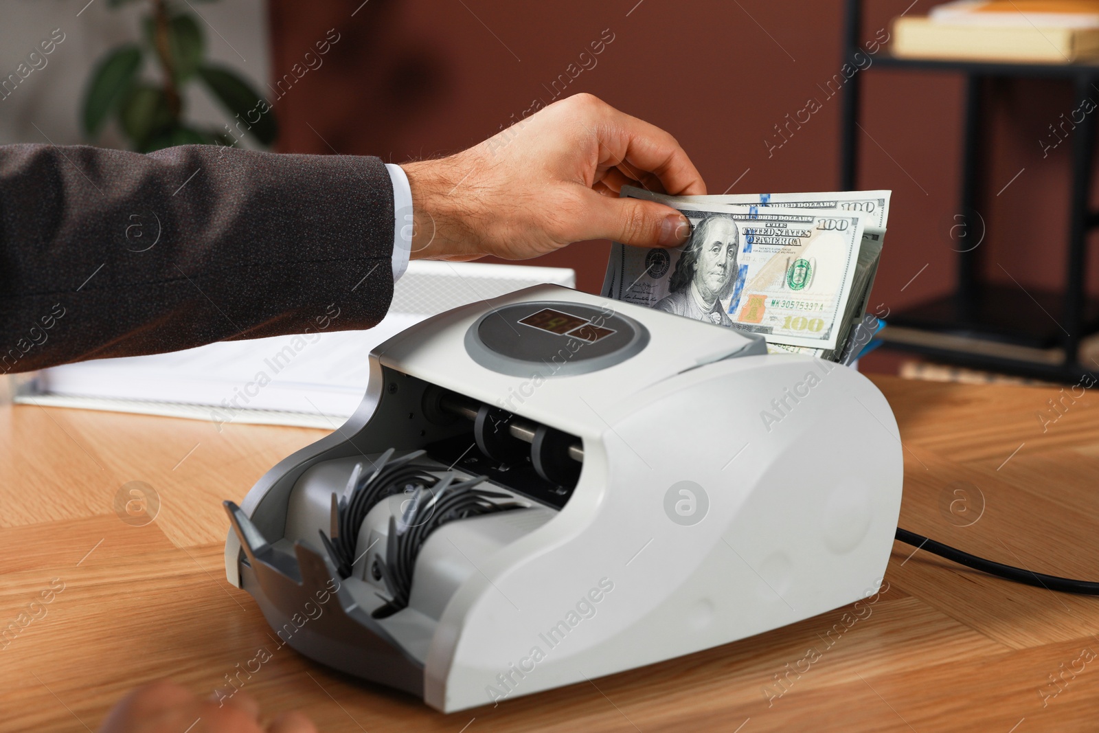 Photo of Man putting money into banknote counter at wooden table indoors, closeup