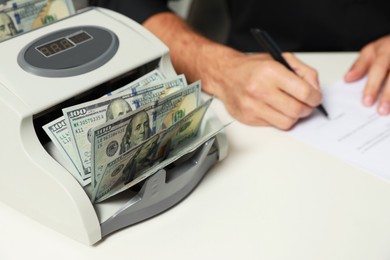 Photo of Modern banknote counter with money and blurred view of man working at white table indoors