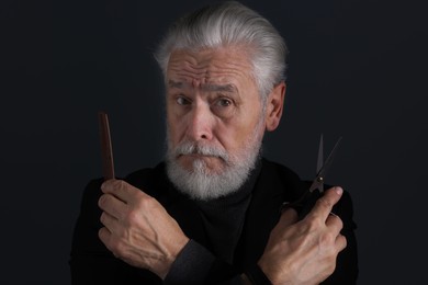 Photo of Bearded man with scissors and comb on dark grey background