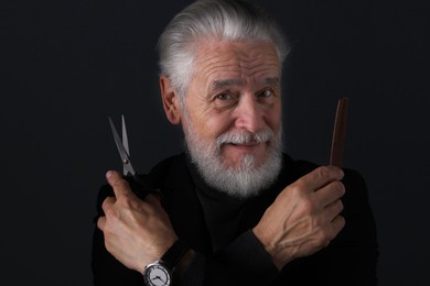 Photo of Bearded man with scissors and comb on dark grey background