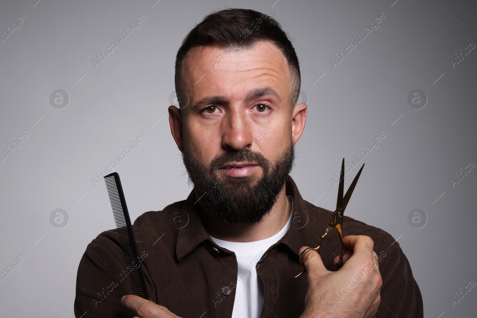 Photo of Bearded man holding comb and scissors on grey background