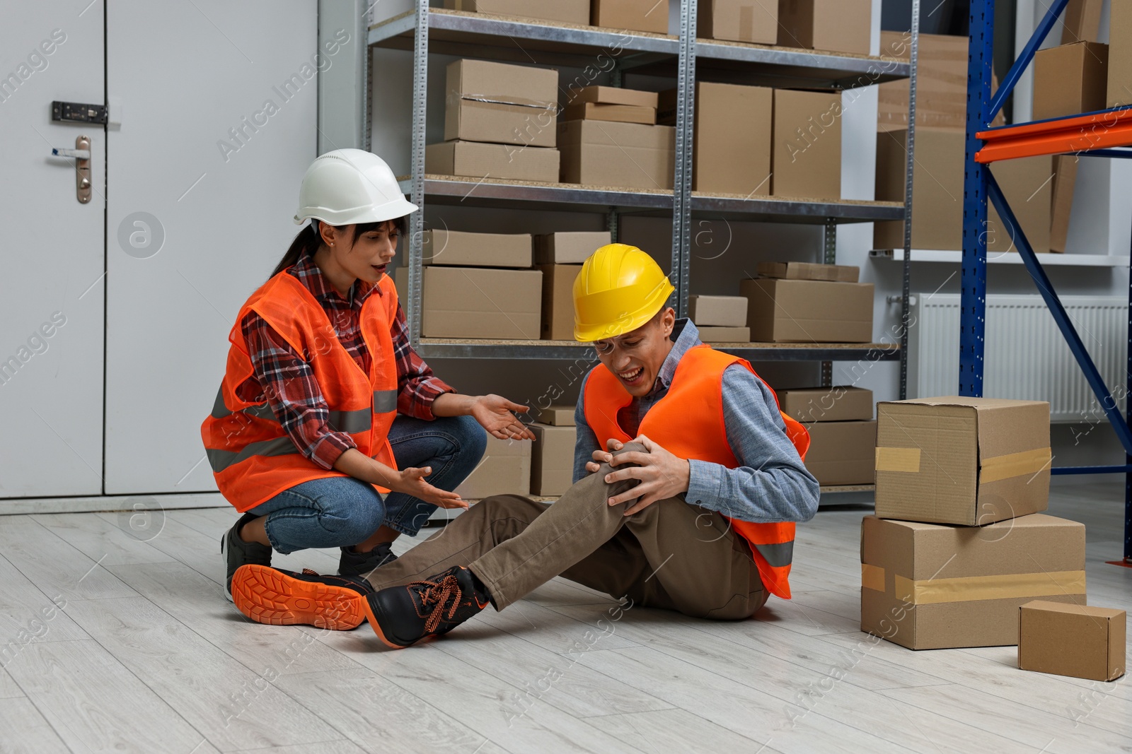 Photo of Accident at work. Woman helping her injured colleague in warehouse