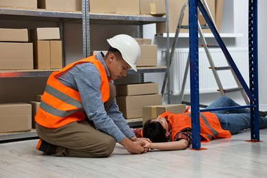 Photo of Accident at work. Man checking pulse of his unconscious colleague in warehouse