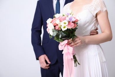 Photo of Bride with beautiful wedding bouquet and groom on light background, closeup. Space for text