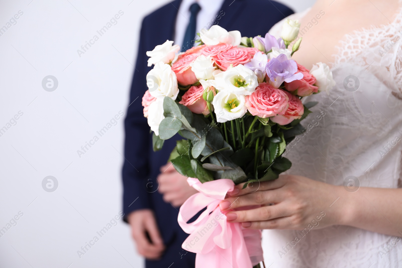 Photo of Bride with beautiful wedding bouquet and groom on light background, closeup. Space for text