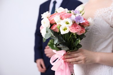 Photo of Bride with beautiful wedding bouquet and groom on light background, closeup. Space for text