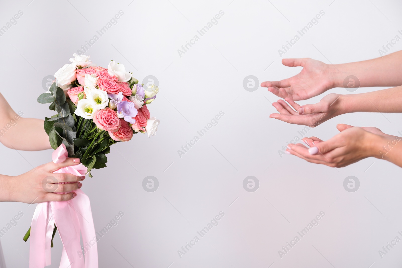 Photo of Bridesmaids giving beautiful wedding bouquet to bride on light background, closeup