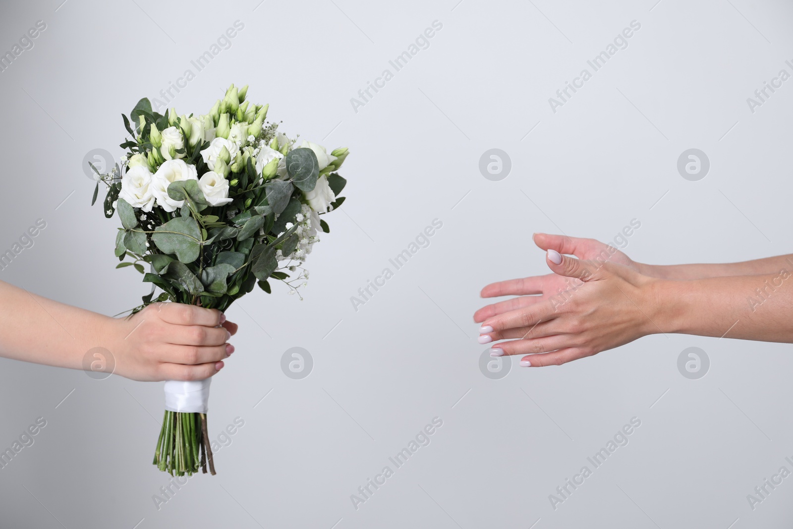 Photo of Bridesmaid giving beautiful wedding bouquet to bride on light background, closeup