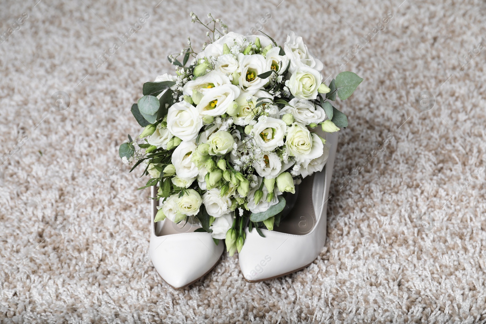 Photo of Wedding bouquet of beautiful flowers and bridal shoes on beige carpet, closeup