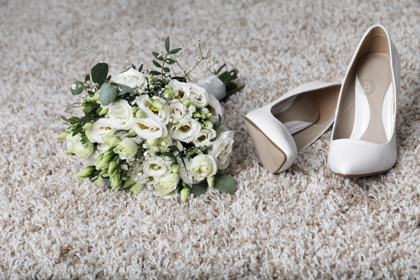 Photo of Wedding bouquet of beautiful flowers and bridal shoes on beige carpet, closeup