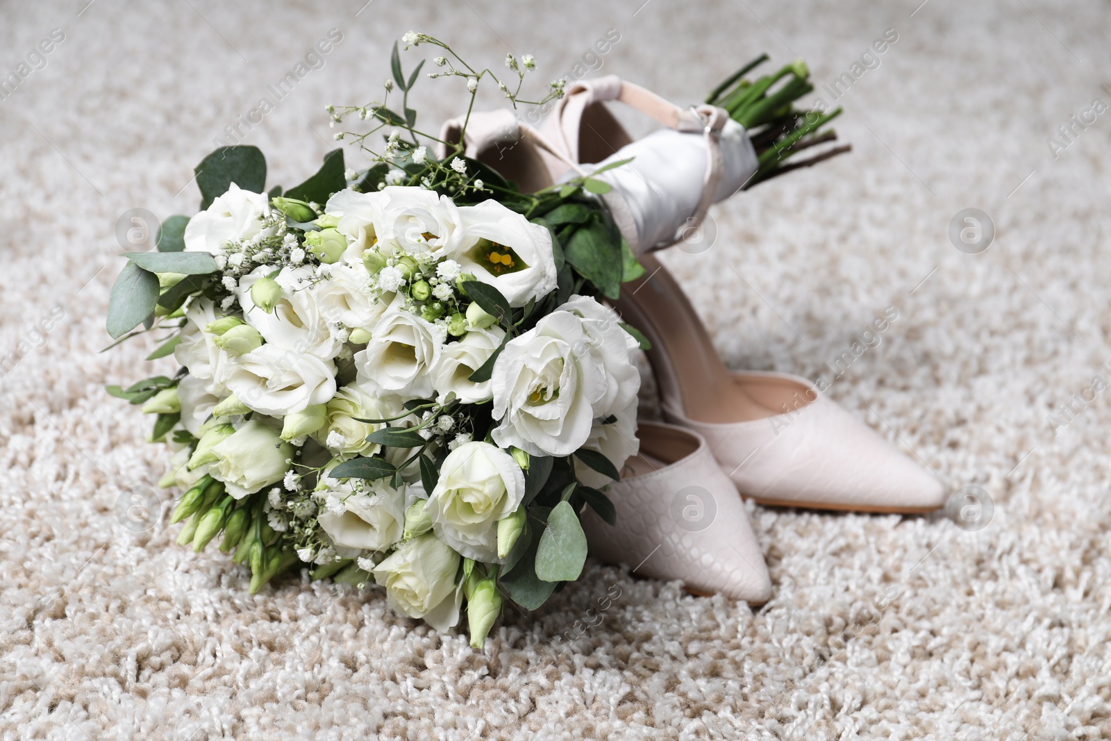 Photo of Wedding bouquet of beautiful flowers and bridal shoes on beige carpet, closeup