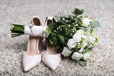 Photo of Wedding bouquet of beautiful flowers and bridal shoes on beige carpet, closeup