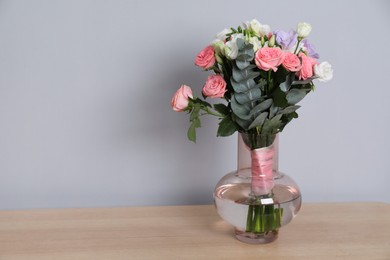 Photo of Wedding bouquet of beautiful flowers in vase on wooden table against grey wall. Space for text