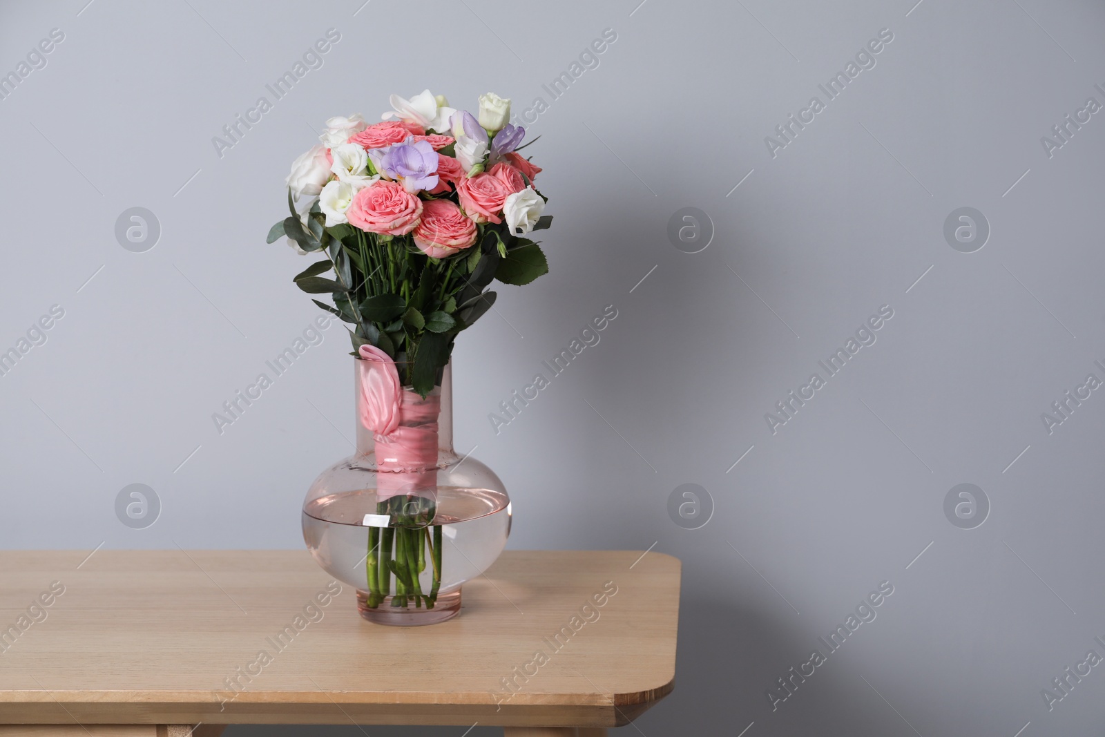 Photo of Wedding bouquet of beautiful flowers in vase on wooden shelf against grey wall. Space for text