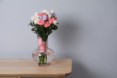 Photo of Wedding bouquet of beautiful flowers in vase on wooden shelf against grey wall. Space for text